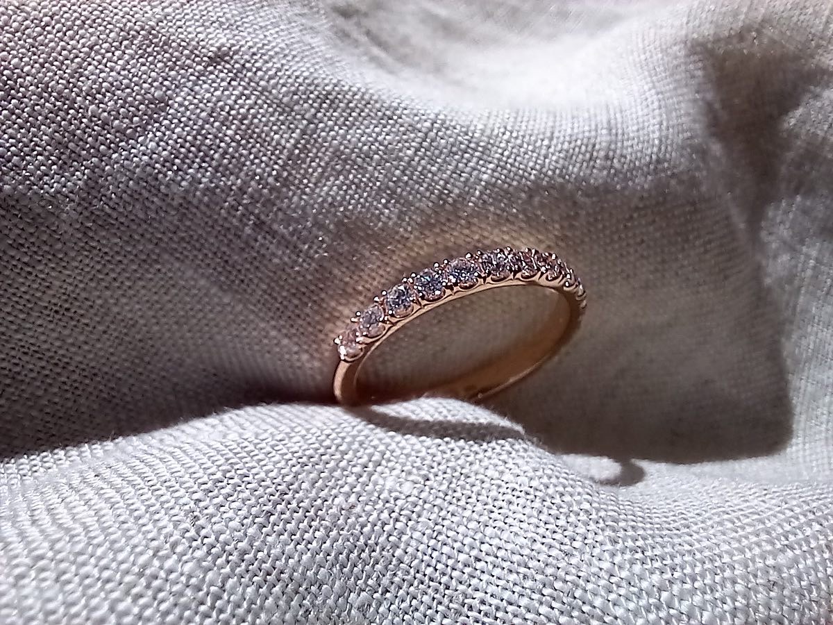 A rose gold band set with a row of small round diamonds across the front, standing upright in folds of pale linen.