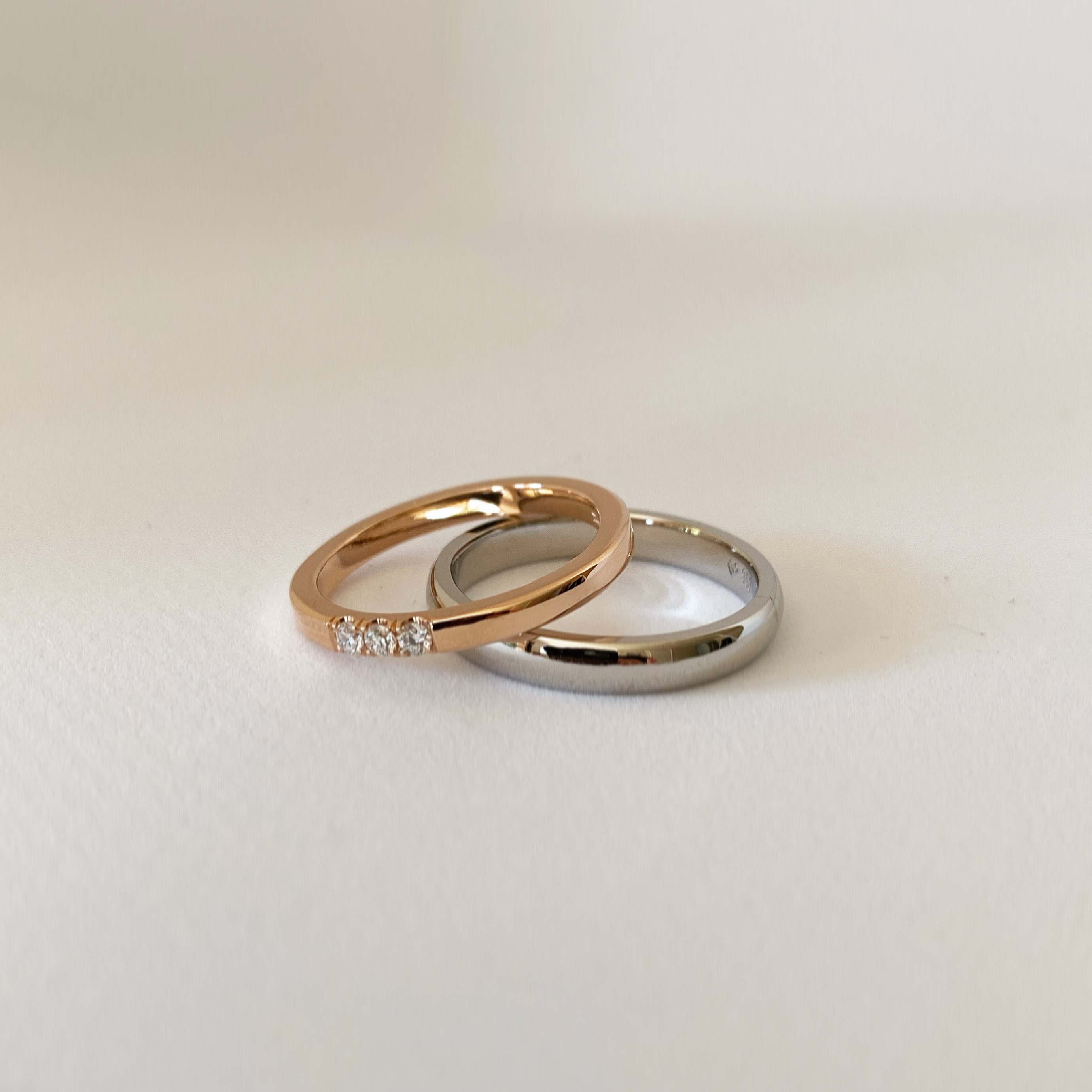 Two wedding bands leaning against each other: a rose gold one set with three small diamonds, and a plain rounded white gold one.