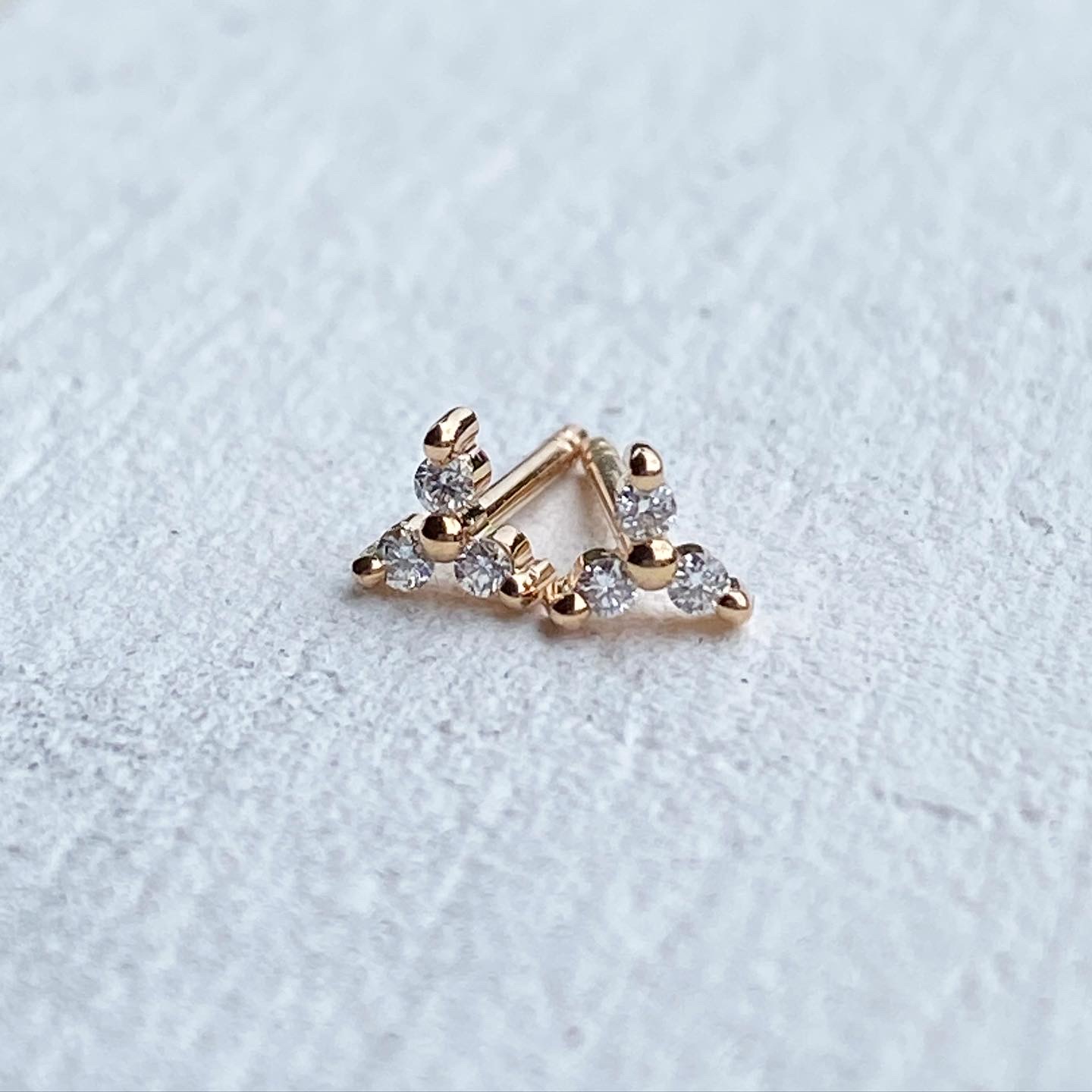 A yellow gold chevron earring set with seven round diamonds following its V shape, standing on a white textured surface.