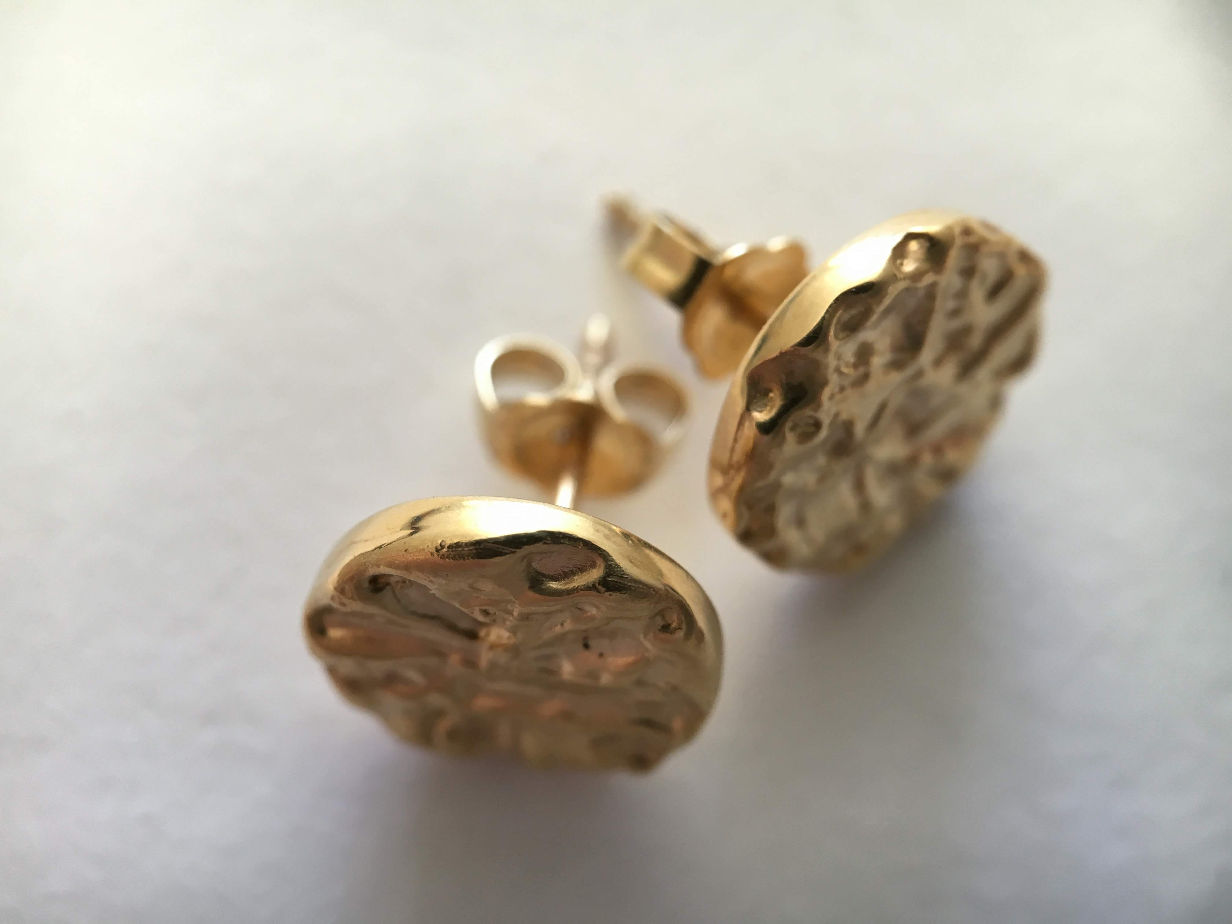 Two round yellow gold stud earrings with a hammered, molten surface, one face-on and one on its side showing the butterfly back.